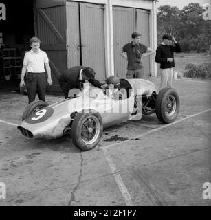 1962, historisch, ein junger männlicher Fahrer sitzt in einem offenen Cooper-Rennwagen und bekommt Unterricht vor einem Schuppen auf dem Finmere-Flugplatz, Finemere, Bucks, England, Großbritannien. zu dieser Zeit der Geoff Clarkes Motor School. Der Cooper-Rennwagen mit seinem Motor hinter dem Fahrer war damals innovativ und gewann als erster Heckmotor ein Formel-1-Rennen. Stockfoto