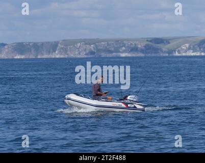 Freizeitangler mit Tablet/ipad beim Angeln auf dem Meer von einem kleinen Boot aus mit Bigbury Bay im Hintergrund Stockfoto