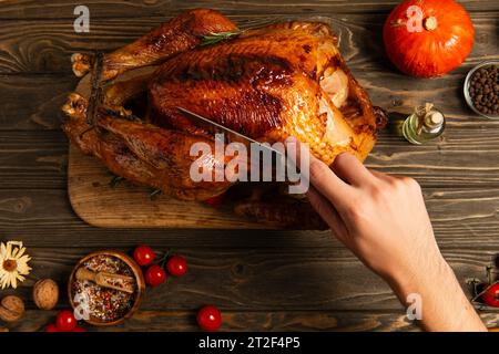 Zugeschnittene Ansicht eines Mannes, der Thanksgiving-truthahn in der Nähe von Kirschtomaten und Kürbis auf Holztisch schneidet Stockfoto