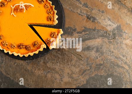 Kuchenspachtel in der Nähe von Thanksgiving Pie, garniert mit Orangenscheiben und Walnüssen auf strukturiertem Steintisch Stockfoto