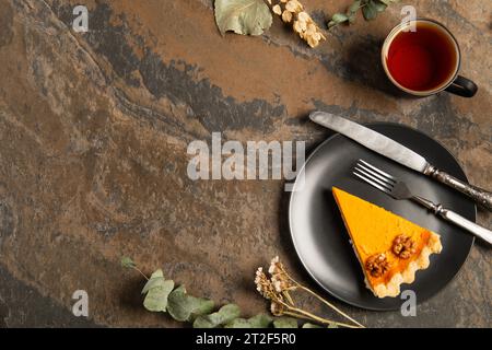 Saisonale Thanksgiving-Einstellung, schwarzer Teller mit Kürbiskuchen in der Nähe von Kräutern und warmer Tee auf Steintisch Stockfoto