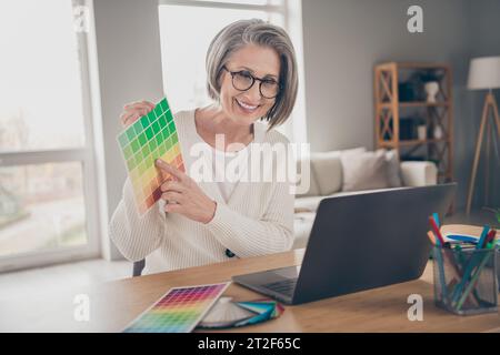 Foto einer süßen glänzenden älteren Designerin tragen weiße Strickjacke mit moderner Farbpalette im Appartementzimmer Stockfoto