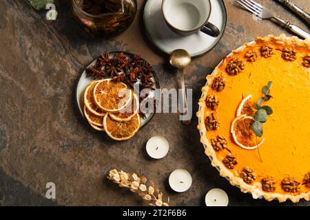 thanksgiving-Thema, garnierter Kürbiskuchen neben Kerzen und Orangenscheiben mit Gewürzen auf Steintisch Stockfoto
