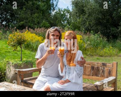 Mann und Frau im Garten auf einer Gartenbank, Gläser mit Fruchtsaft in der Hand, Deutschland Stockfoto