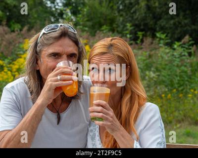 Mann und Frau im Garten mit frisch gepresstem Fruchtsaft, Paar mit Trinkgläsern in der Hand trinken, Deutschland Stockfoto