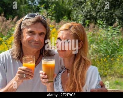 Mann und Frau im Garten mit frisch gepresstem Fruchtsaft, Paar mit Trinkgläsern in der Hand trinken, Deutschland Stockfoto
