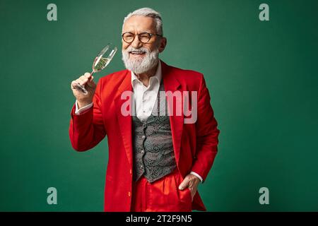 Fröhlicher Mann als Weihnachtsmann gekleidet und genießt ein Glas Champagner mit einer Hand in der Tasche, Winterkonzept Stockfoto