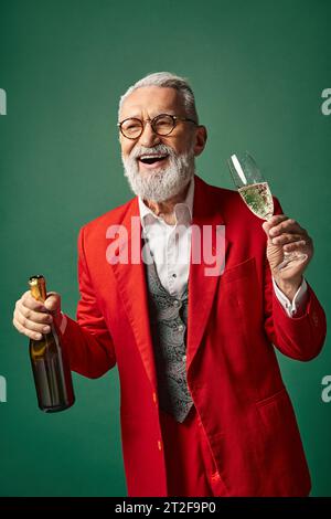 Fröhlicher Mann als Weihnachtsmann gekleidet mit Bart, der Champagner genießt und aufrichtig lächelnd, Winterkonzept Stockfoto