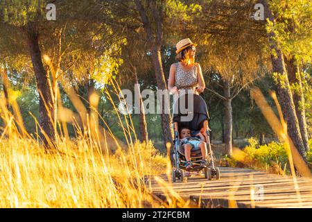 Eine junge Frau, die bei Sonnenuntergang mit ihrem Sohn auf dem Holzweg im Donana Naturpark spaziert. Huelva Stockfoto