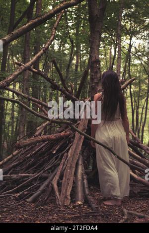 Eine Frau in einem weißen Kleid im tiefen Wald, eine Hexe, eine wilde Frau, die im Wald lebt, ein klassisches weißes Kleid Stockfoto