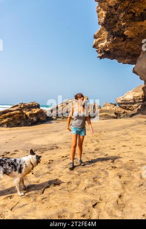 Eine junge Frau, die mit dem Hund am Meer in Playa de Garcey, Westküste von Fuerteventura, den Kanarischen Inseln, spaziert. Spanien Stockfoto