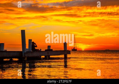 Roatan, Honduras Â», Januar 2020: Ein junger Mann, der den Sonnenuntergang von Roatan auf einem hölzernen Dock im West End fotografiert Stockfoto