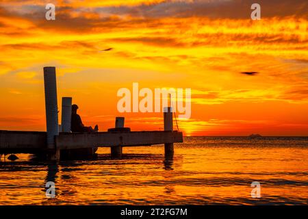 Roatan, Honduras Â», Januar 2020: Ein junger Mann, der den Sonnenuntergang von Roatan auf einem hölzernen Dock im West End fotografiert Stockfoto