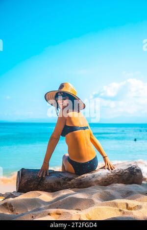 Tela, Honduras Â», Januar 2020: Ein Blick auf eine junge Frau mit Hut, die auf einem Baumstamm am Strand von Punta Sal in Tela sitzt Stockfoto