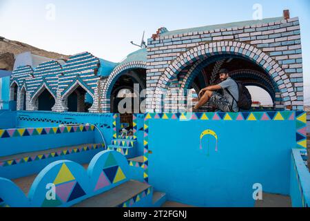 Ein junger Tourist, der auf einer wunderschönen Terrasse eines traditionellen blauen Hauses in einem nubischen Dorf am Nil und in der Nähe der Stadt Assuan sitzt. Ägypten Stockfoto