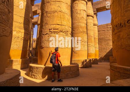 Ein junger Tourist, der zwischen den Säulen mit Hieroglyphen im Tempel von Karnak, dem großen Heiligtum von Amun, spaziert. Ägypten Stockfoto