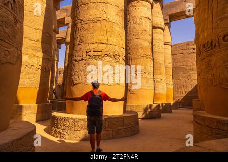 Ein junger Tourist, der zwischen den Säulen mit Hieroglyphen im Tempel von Karnak, dem großen Heiligtum von Amun, spaziert. Ägypten Stockfoto