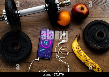 Draufsicht auf Workout- und Fitness-Hantel, frisches Obst und Smartphone mit Gesundheits- und Fitness-App auf dem Bildschirm. Wellness, Diät und häusliche Körperpflege Co Stockfoto