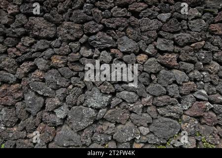 Eine Mauer aus dunklen, vulkanischen Bimsfelsen wird in einer Nahaufnahme gezeigt, Außenansicht während des Tages. Stockfoto