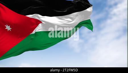 Die Nationalflagge Jordaniens winkt an einem klaren Tag im Wind. Schwarze, weiße und grüne horizontale Streifen mit einem roten Chevron auf der linken Seite mit einem weißen s Stockfoto