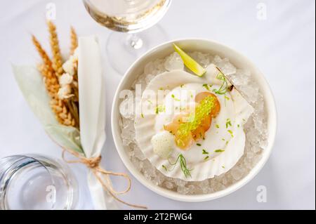 Jakobsmuschel in Soße mit fliegenden Fischkaviar auf einer Schale auf Eis in einem Restaurant. Hochwertige Fotos Stockfoto