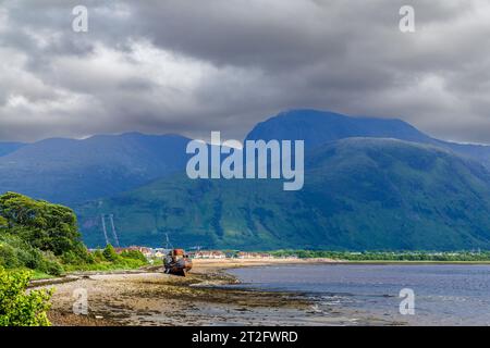 Ein ruchloses Fischerboot am Ufer des Loch Linnhe, dem Dorf Caol und Ben Nevis dahinter, von Corpach am Caledonian Canal in Westschottland Stockfoto