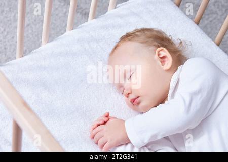 Das Baby schläft sicher und süß in seiner Holzkrippe auf einem Frottee-Laken mit einem Gummiband. Das Kleinkind schläft im Bett-Bett-Bett. Sicheres Mitschlafen Stockfoto