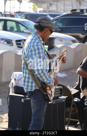 Ein Foto eines alten, nicht erkennbaren Mannes, der auf den Gehwegen am venice Beach Gitarre spielt. Stockfoto