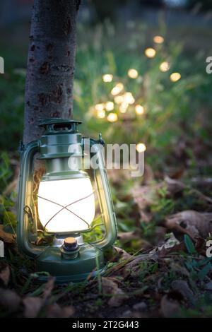Vintage-Metall-Öllampe oder Laterne, die im Dunkeln auf dem Gras leuchtet, Camping-Hintergrund mit Kopierraum. Vertikale Aufnahme. Stockfoto