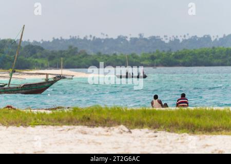 Afrikanische Fischer, die am Sandstrand sitzen, blicken auf das Meer, bewölkter Tag, Sansibar, Tansania. Stockfoto