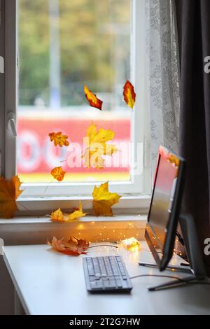 Computer nahe herbstlicher Blätter am Fenster Stockfoto