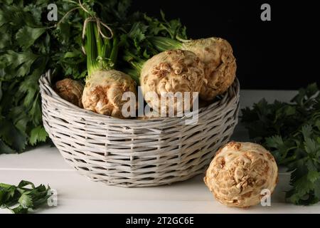 Fresh raw celery roots in wicker basket on white wooden table Stock Photo