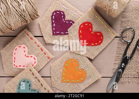 Stücke Sackleinen-Stoff mit Herzen und Schere auf Holztisch, flach gelegt Stockfoto