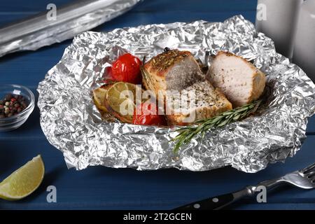 Köstliche Fleischstücke in Folie gebacken mit Tomaten auf blauem Holztisch Stockfoto