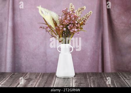Künstliche Blumen in weißer Vase auf rosa Stoffhintergrund. Stockfoto