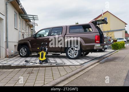 Ein sauberes Auto steht in der Nähe der Garage, daneben befindet sich ein Gerät zum Waschen des Autos unter fließendem Wasser. Es gibt ein Haus im Hintergrund. Stockfoto