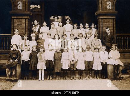 Ein viktorianisches oder edwardianisches Klassenfoto von amerikanischen Schulkindern und ihrem Lehrer. Einschließlich eines kleinen schwarzen Jungen in der ersten Reihe. Stockfoto