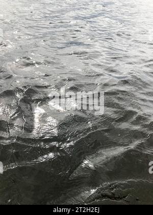 Textur von dunklem schwarzem kaltem Wasser mit Wellen von Wellen von Wellen, die sich kräuseln. Der Hintergrund. Stockfoto