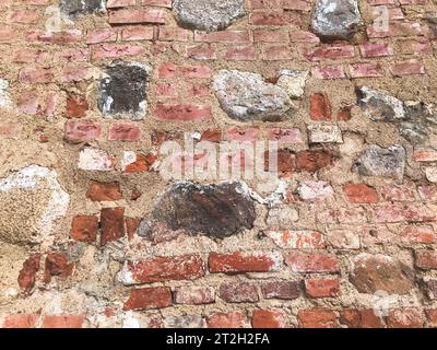 Die Textur des alten antiken mittelalterlichen antiken Steins, der hart abblättert, zerrissene Ziegelwand aus rechteckigen roten Tonziegeln und großen Steinen, Kopfsteinpflaster. T Stockfoto