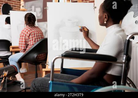 Junge schwarze Frau mit körperlicher Behinderung, Besuchergruppen-Zeichenwerkstatt, kreative Therapie für behinderte Erwachsene, Kunst in der körperlichen Rehabilitation. Afroamerikanisches Mädchen Rollstuhlzeichnung auf Leinwand Stockfoto