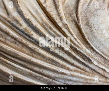 Antike Textur. Beiger Stein, voluminöser Hintergrund. Eine Statue in Gewändern, ein Stück Marmortuch. Rostiger weißer Hintergrund. Stockfoto