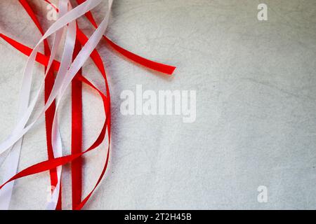 Textur mit roten und weißen schönen festlichen Bändern aus einem künstlichen Stoff auf hellgrauem Hintergrund. Der Hintergrund. Stockfoto
