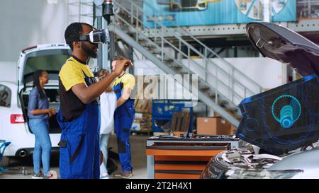 Qualifizierter Techniker in der Werkstatt, der fortschrittliche Virtual-Reality-Technologie verwendet, um mechanische Komponenten des Fahrzeugs zu visualisieren und zu reparieren. Garagenexperte trägt vr-Brille bei der Reparatur beschädigter Fahrzeuge Stockfoto