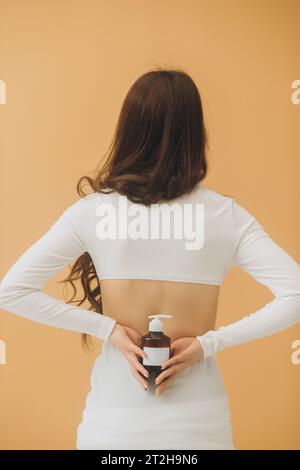 Eine Frau hält eine Flasche Kosmetik in der Hand und steht mit dem Rücken zur Kamera. Kosmetikmodell. Stockfoto