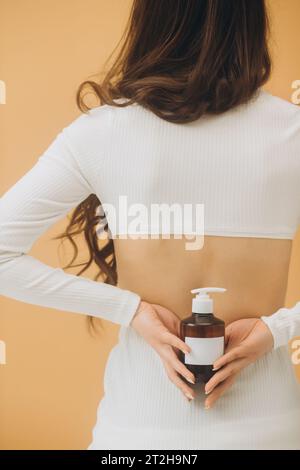 Eine Frau hält eine Flasche Kosmetik in der Hand und steht mit dem Rücken zur Kamera. Kosmetikmodell. Stockfoto