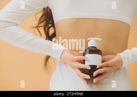 Eine Frau hält eine Flasche Kosmetik in der Hand und steht mit dem Rücken zur Kamera. Kosmetikmodell. Stockfoto