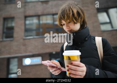 Niedliches Teenager-Mädchen mit Kaffee zum Mitnehmen am kalten Wintertag. Teenager-Kind trinkt heißes Getränk an kühlen Tagen. Stockfoto