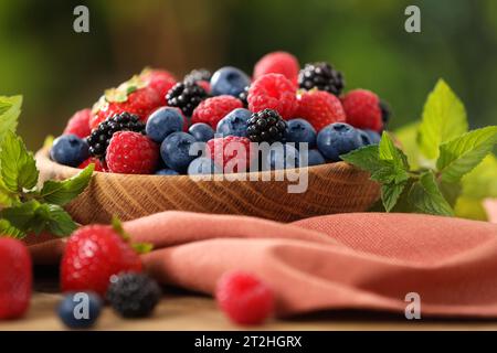 Schüssel mit verschiedenen frischen Reifen Beeren und Minze auf Tisch draußen, Nahaufnahme Stockfoto