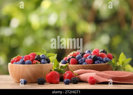 Schüsseln mit verschiedenen frischen, Reifen Beeren und Minze auf dem Tisch draußen Stockfoto