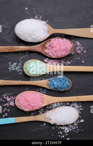 Löffel mit verschiedenen Meersalzen auf schwarzem Tisch, flach gelegt Stockfoto